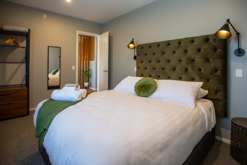 Bedroom in The Residence three-bedroom spa apartment, with white bedding and a green upholstered headboard